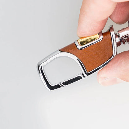 Cognac leren sleutelhanger tussen duim en wijsvinger, messingkleurige knop bovenop