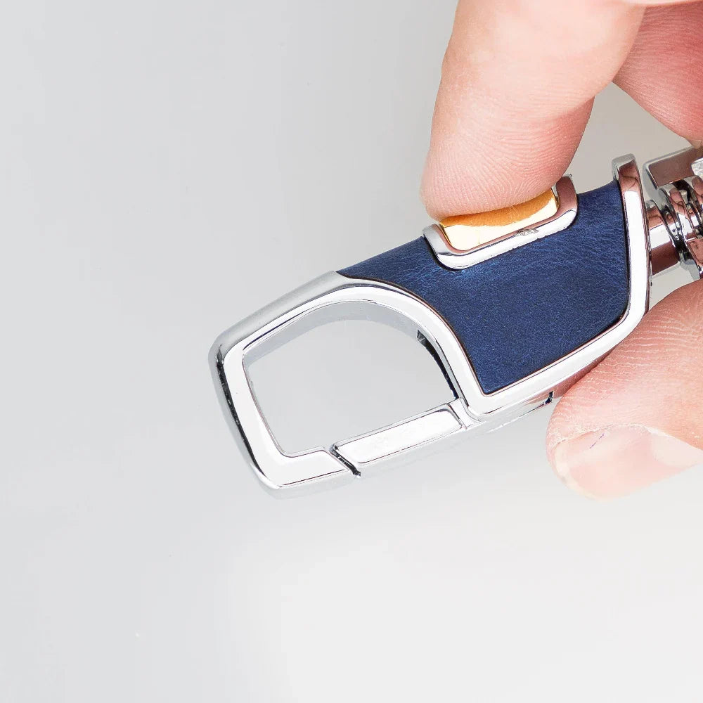 Cadetblauwe leren sleutelhanger in de hand, messingkleurige duimknop op het leerpaneel