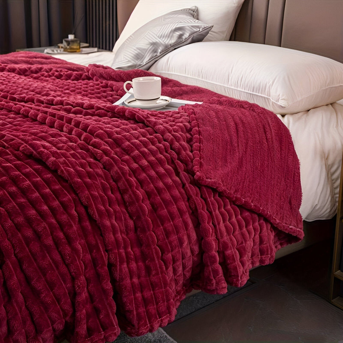 Fleece deken van koraalfleece met blokjesreliëf over een bed - wijnrood