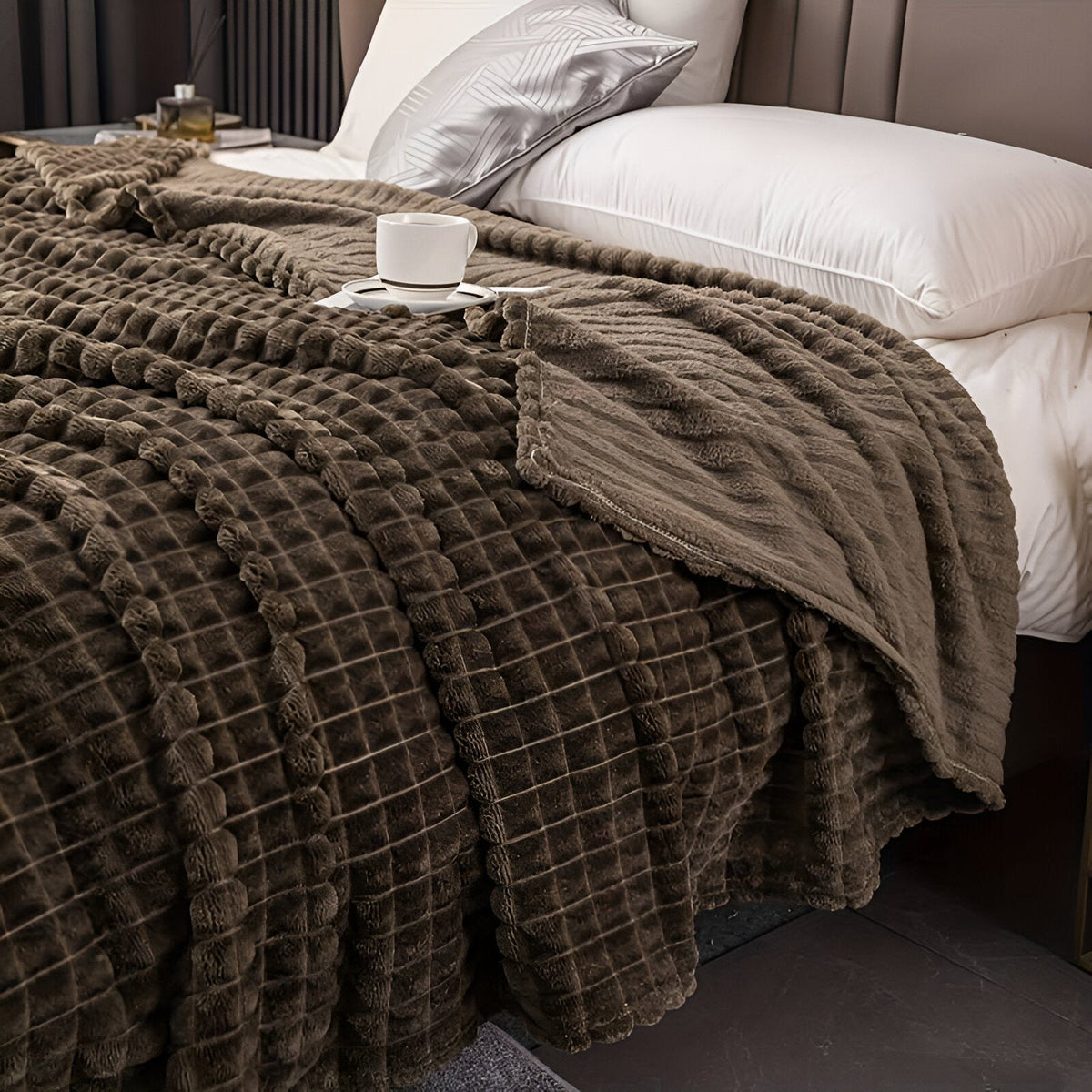Fleece deken van koraalfleece met blokjesreliëf over een bed - taupe