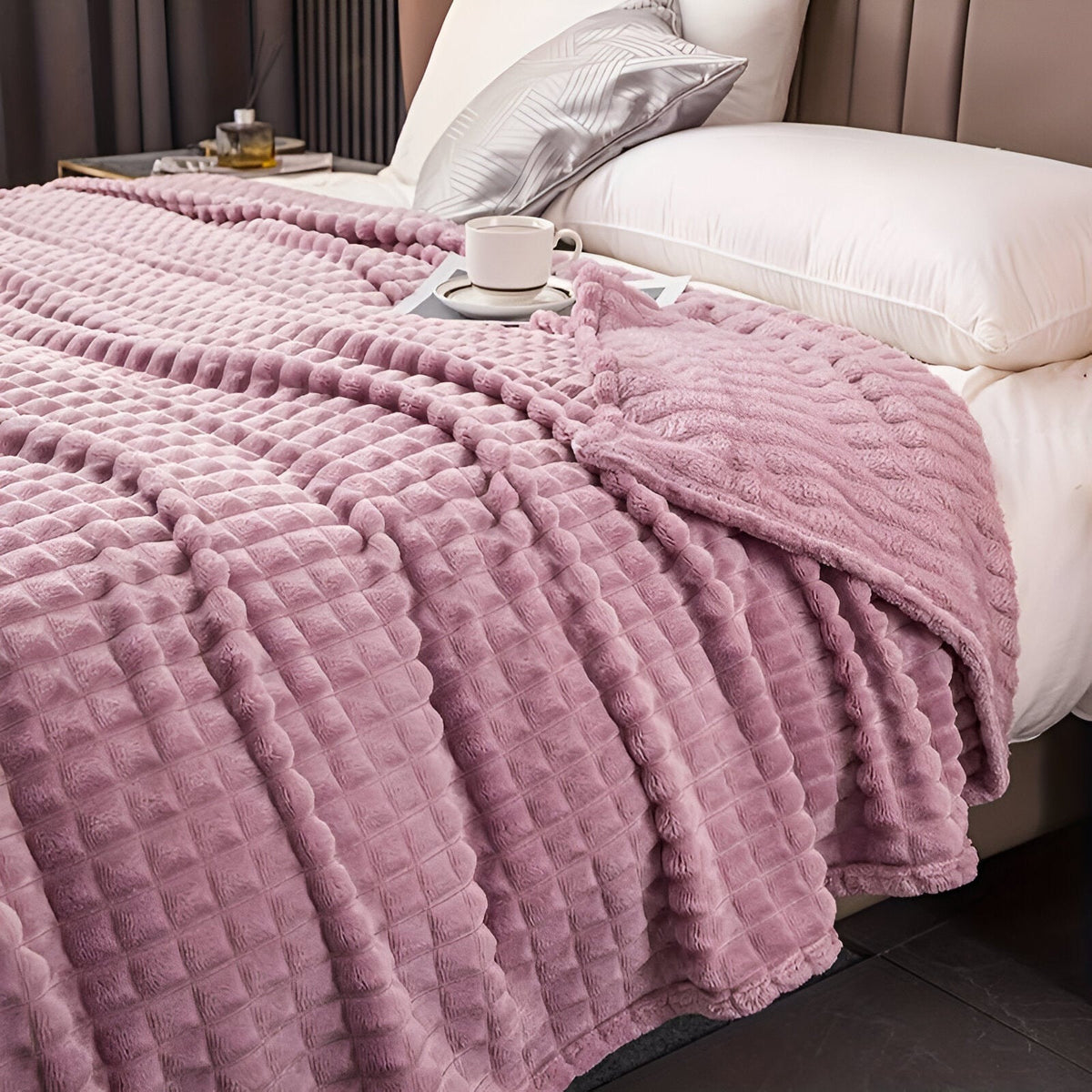 Fleece deken van koraalfleece met blokjesreliëf over een bed - mauve
