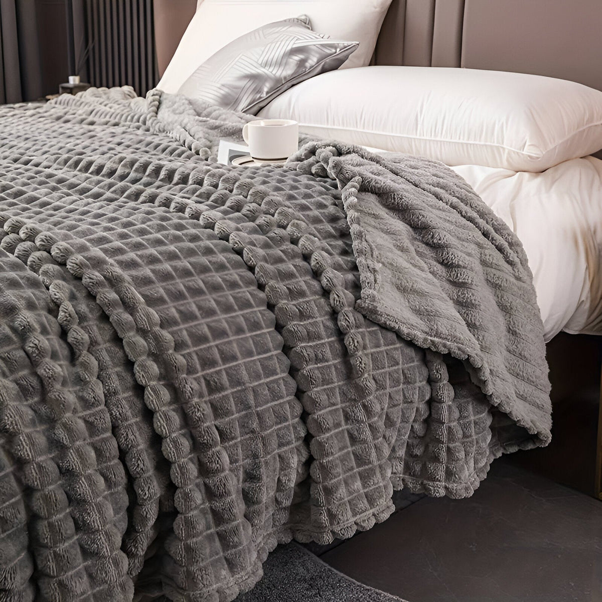 Fleece deken van koraalfleece met blokjesreliëf over een bed - donkergrijs