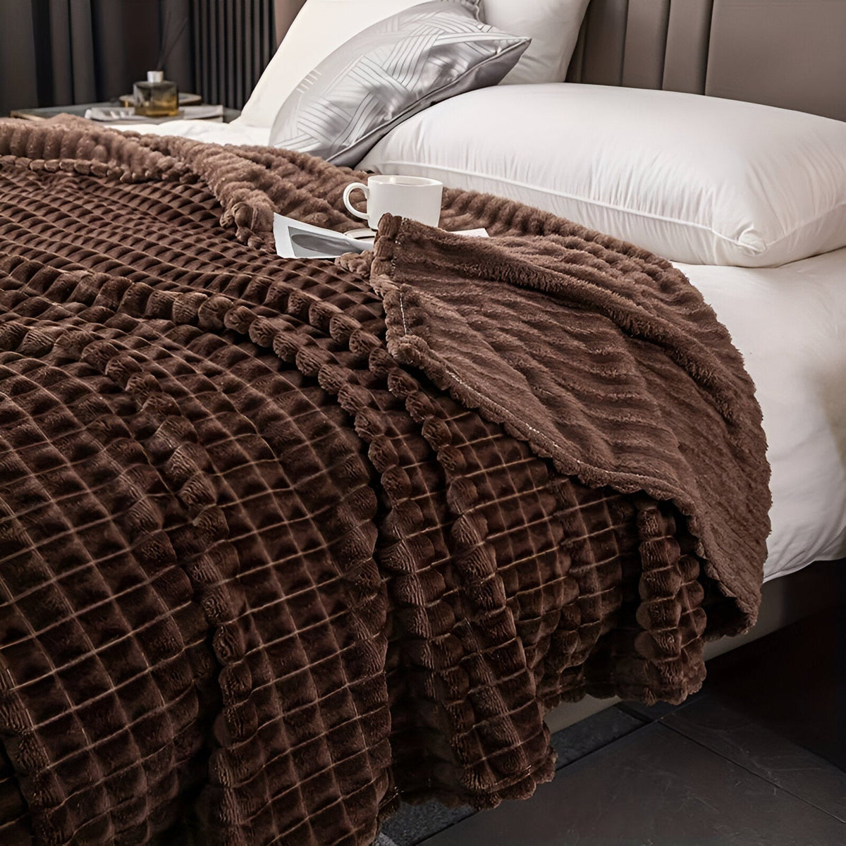 Fleece deken van koraalfleece met blokjesreliëf over een bed - chocoladebruin