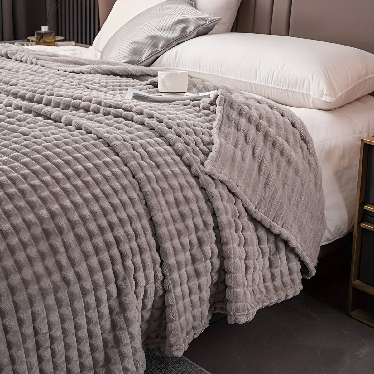 Fleece deken van koraalfleece met blokjesreliëf over een bed - lichtgrijs