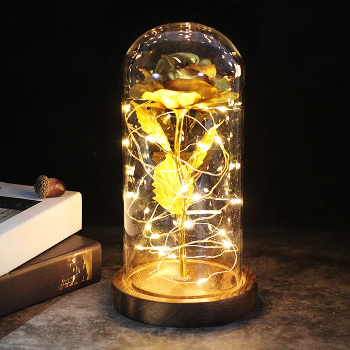 Kunstroos onder een doorzichtige stolp met LED-lichtsnoer om de steel, op een ronde houten voet - goud