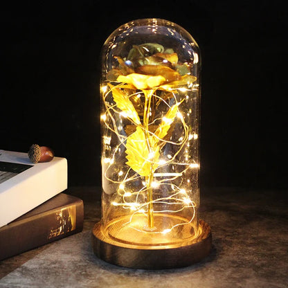 Kunstroos onder een doorzichtige stolp met LED-lichtsnoer om de steel, op een ronde houten voet - goud