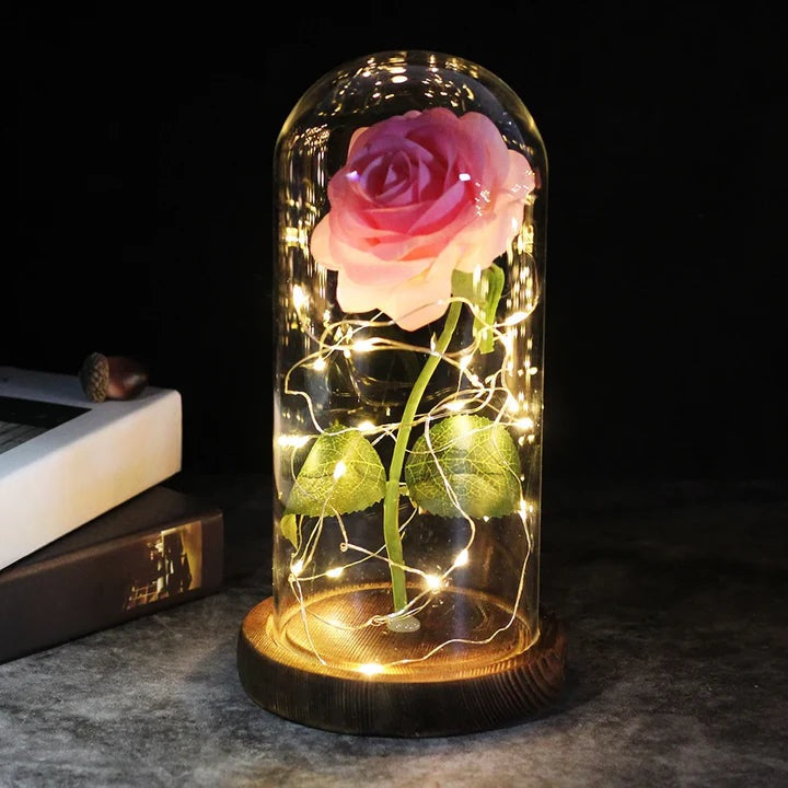 Kunstroos onder een doorzichtige stolp met LED-lichtsnoer om de steel, op een ronde houten voet - roze