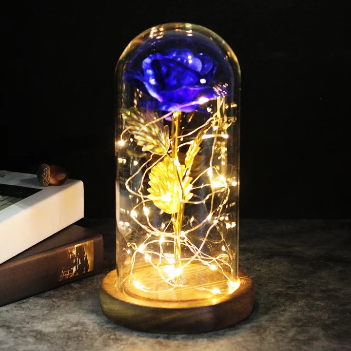 Kunstroos onder een doorzichtige stolp met LED-lichtsnoer om de steel, op een ronde houten voet - blauw