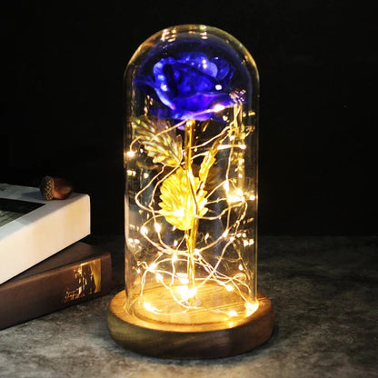 Kunstroos onder een doorzichtige stolp met LED-lichtsnoer om de steel, op een ronde houten voet - blauw