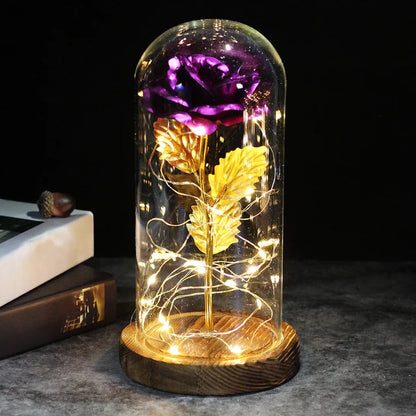 Kunstroos onder een doorzichtige stolp met LED-lichtsnoer om de steel, op een ronde houten voet - paars