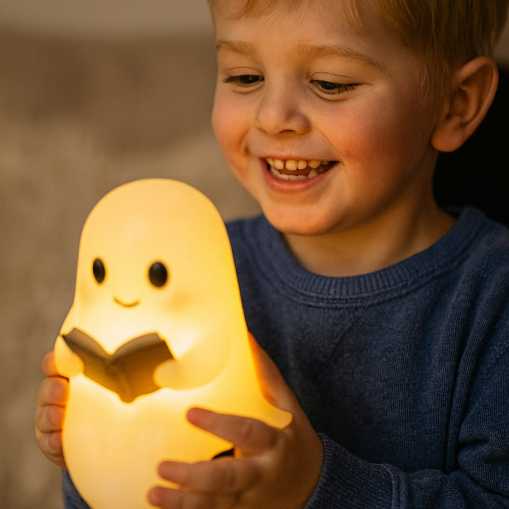 Wit spooklampje met zwarte oogjes en roze wangen dat een open bruin boek vasthoudt en warm geel oplicht