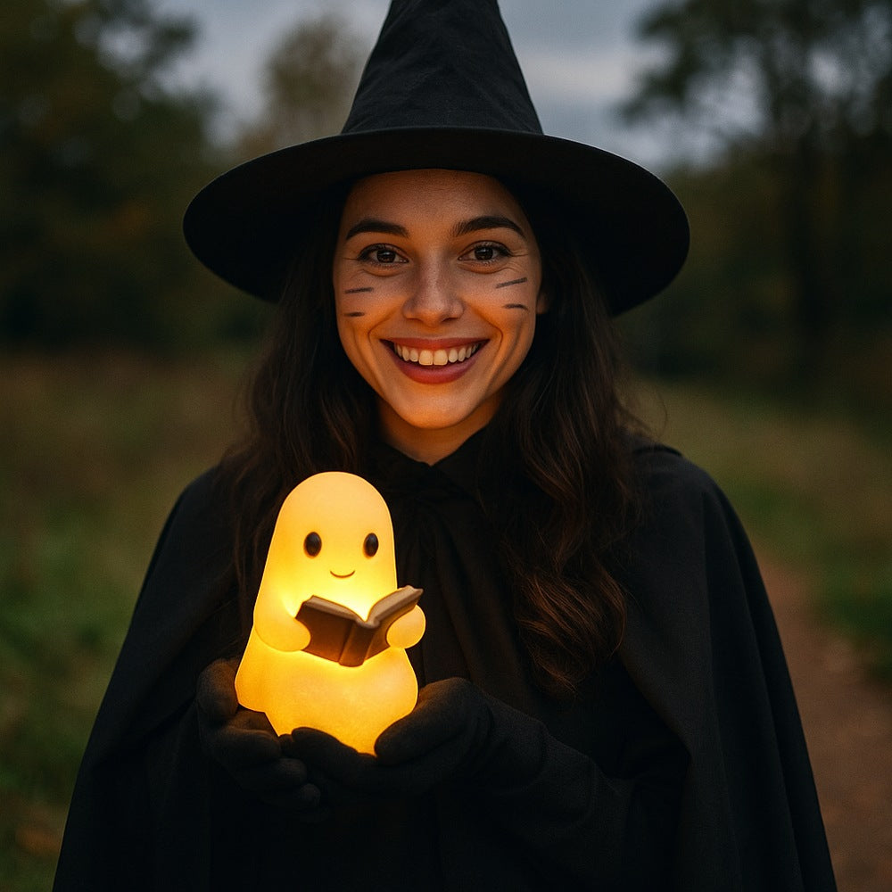 Wit spooklampje met zwarte oogjes en roze wangen dat een open bruin boek vasthoudt en warm geel oplicht