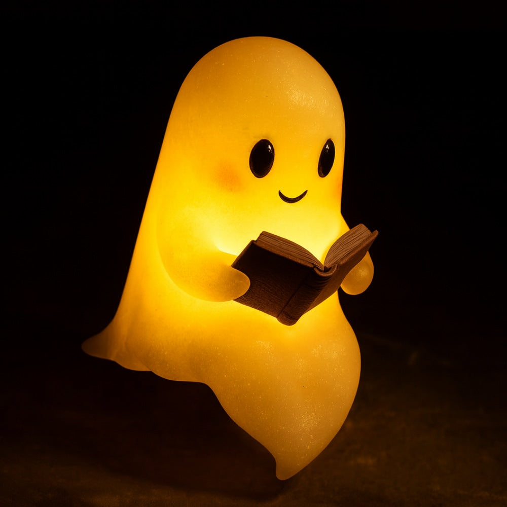 Wit spooklampje met zwarte oogjes en roze wangen dat een open bruin boek vasthoudt en warm geel oplicht