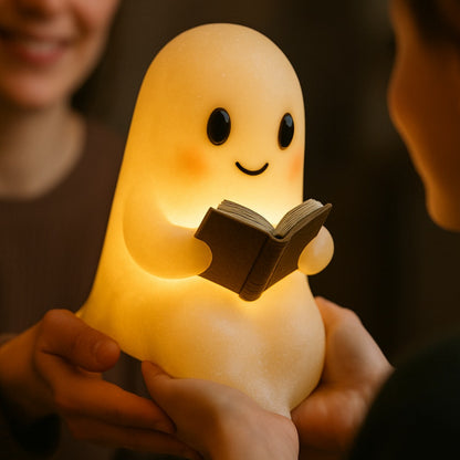 Wit spooklampje met zwarte oogjes en roze wangen dat een open bruin boek vasthoudt en warm geel oplicht