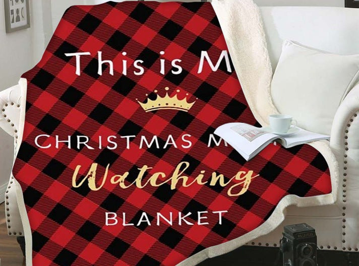 Kerstplaid met teddy achterkant en kerstprint over een fauteuil - rood-zwart geruit met kerstfilmtekst