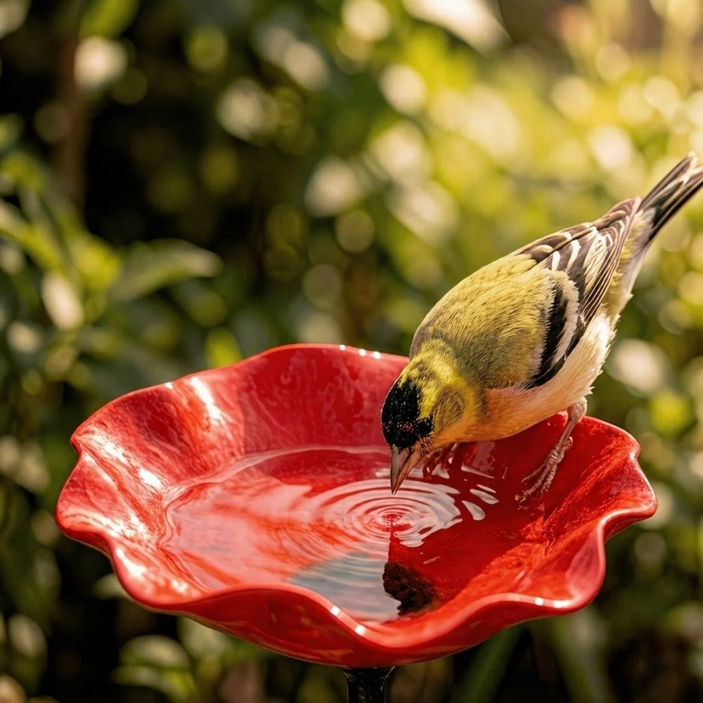 Rood vogelbad in bloemvorm met golvende rand op een metalen steel tussen bloeiende tuinplanten