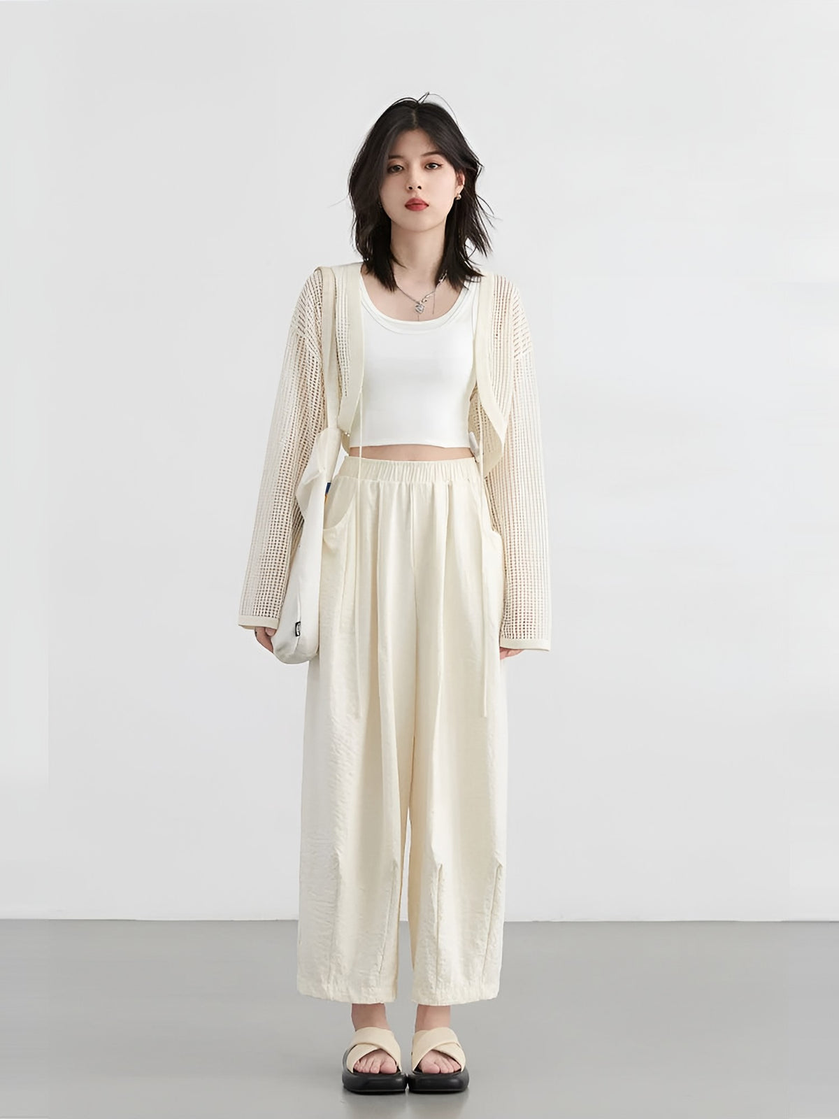 Model in een crème wijde damesbroek met wit topje en vest